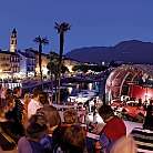 Pubblico assiste a un concerto in riva al lago di sera.