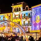 Piazza illuminata da proiezioni colorate e persone che si godono l&#039;atmosfera.