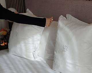 Una persona sistema cuscini bianchi su un letto elegante.