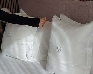 Una persona sistema cuscini bianchi su un letto elegante.