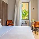 Interno di una camera con letto, sedie e finestra con piante.