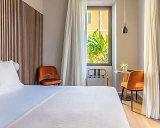 Intérieur d&#039;une chambre avec lit, chaises et fenêtre sur jardin.