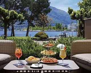 A table set with food and drinks overlooking a lake and mountains.